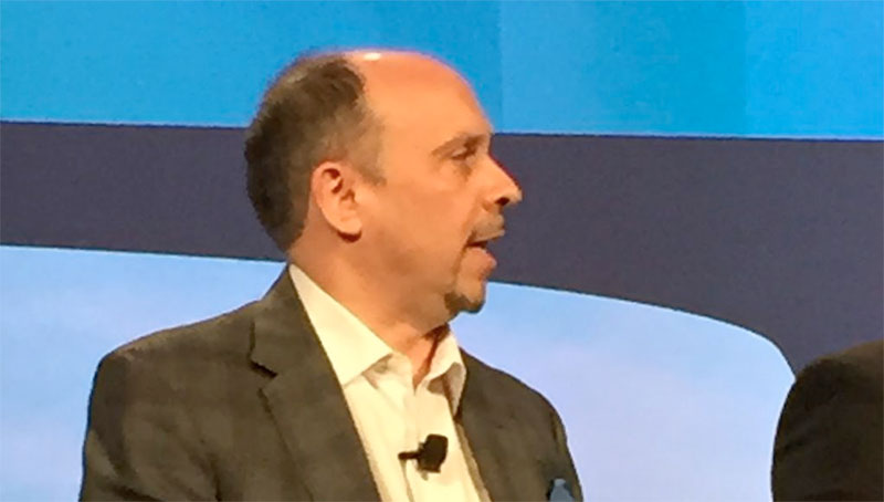 Jamie on a panel discussion in suit with lapel microphone addressing others on the stage.